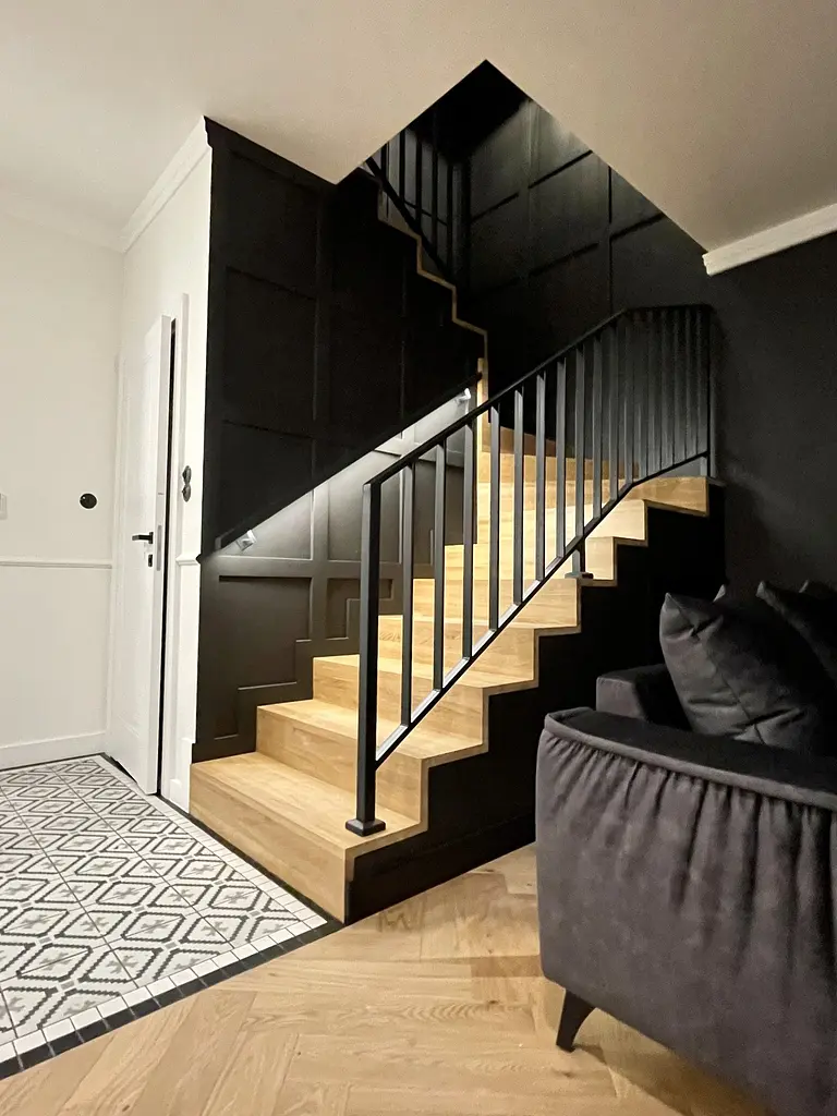 Korytarz w stylu art deco z drewnianymi schodami, czarnymi ścianami i industrialnym wykończeniem.