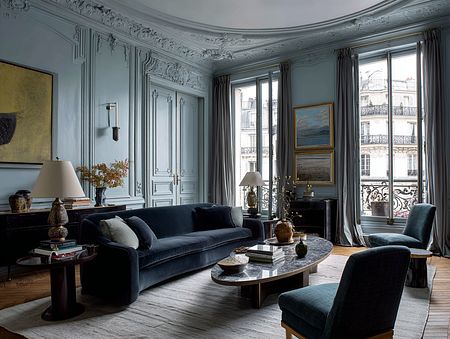 Wnętrze salonu z niebieskimi ścianami, ciemnymi meblami i lampą, styl quiet luxury.