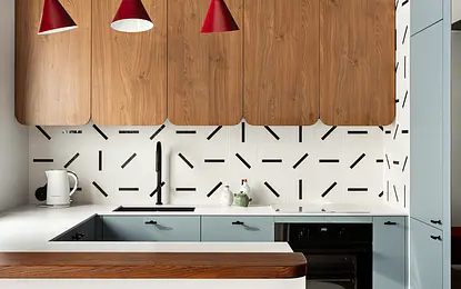 Wnętrze kuchni z drewnianymi szafkami, białym blatem i czerwonymi lampami w stylu dopamine decor.