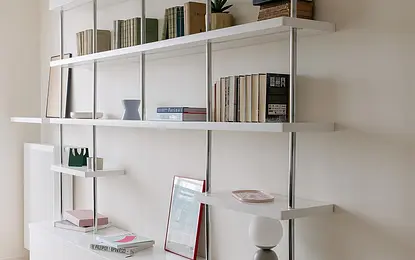 Minimalistyczne wnętrze z białymi półkami, książkami i nowoczesnym oświetleniem.