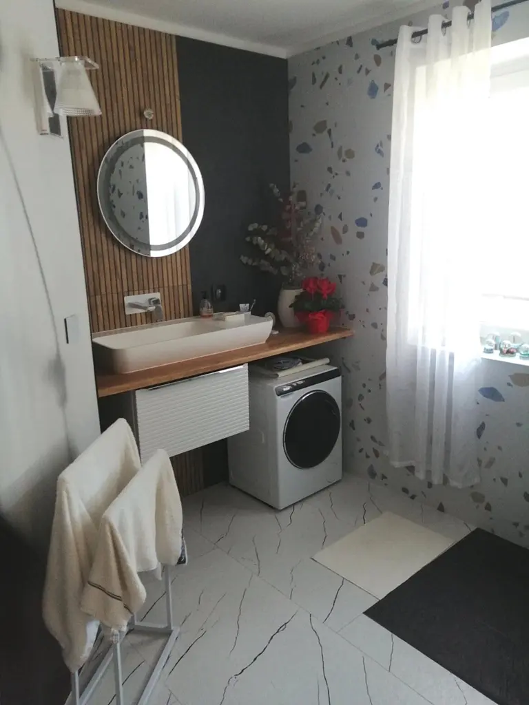 Wnętrze łazienki z nowoczesną umywalką, pralką i drewnianymi akcentami.