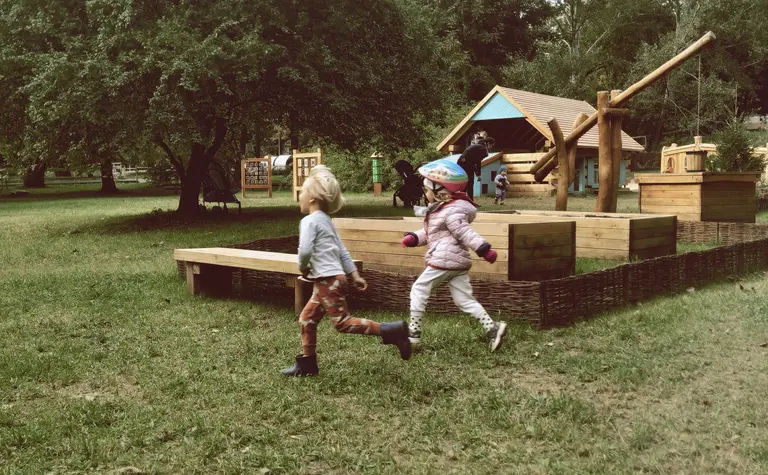 Dzieci bawiące się na placu zabaw w otoczeniu zieleni, tradycyjny styl.
