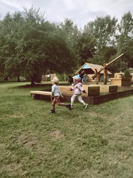 Dzieci bawiące się na placu zabaw w otoczeniu zieleni, tradycyjny styl.
