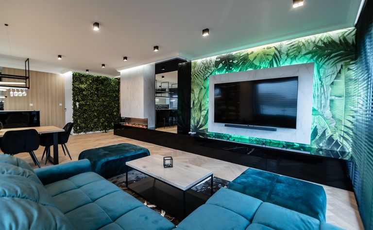 Nowoczesny salon z zielonymi roślinami, telewizorem i elegancką sofą.