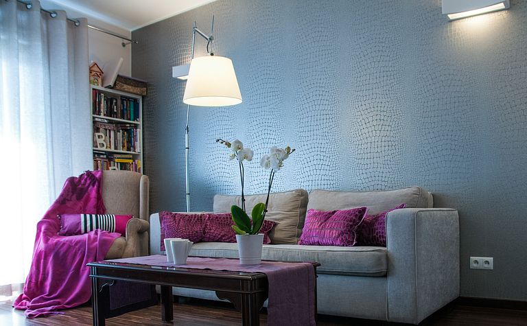 Wnętrze salonu z szarymi ścianami, fioletowymi poduszkami i białymi orchideami.