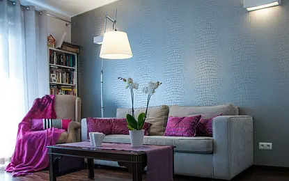 Wnętrze salonu z szarymi ścianami, fioletowymi poduszkami i białymi orchideami.