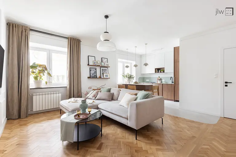 Wnętrze salonu w stylu art deco i skandynawskim z beżową sofą, drewnianym stołem i roślinnością.