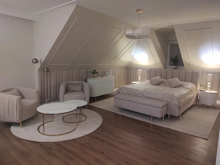Sypialnia w stylu glamour z jasnym łóżkiem, lampami i eleganckim wystrojem.