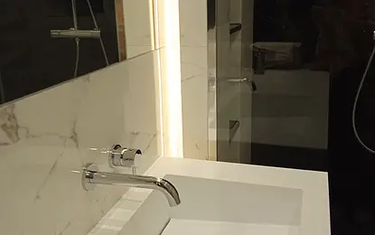 Minimalistyczna łazienka z białą umywalką i nowoczesnym oświetleniem.