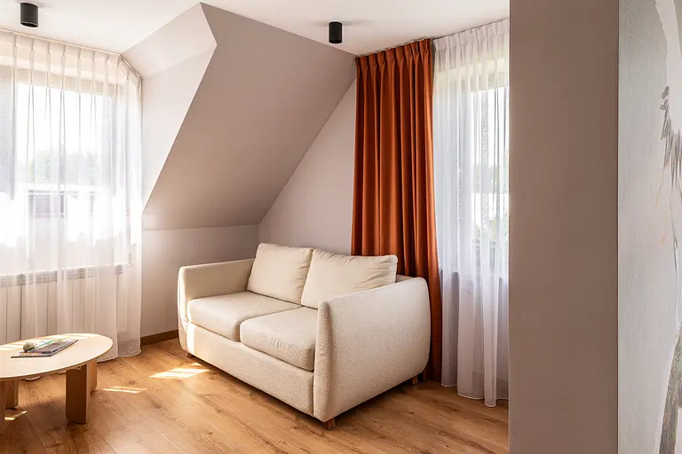 Wnętrze poddasza z beżową sofą, pomarańczowymi zasłonami w stylu boho i skandynawskim.