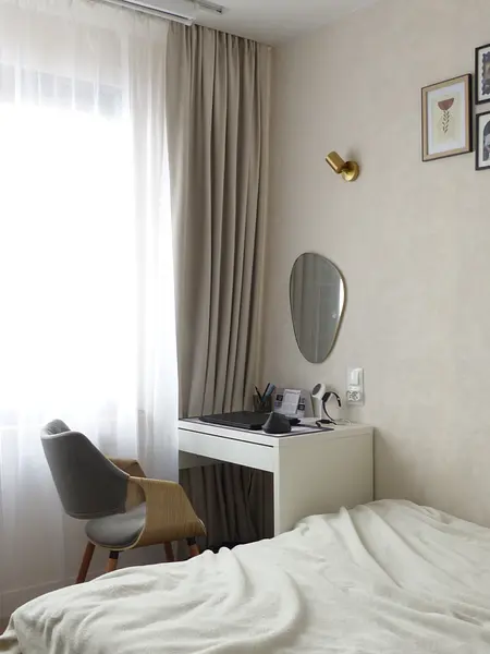 Minimalistyczny pokój z biurkiem, lustrem i jasnymi zasłonami.