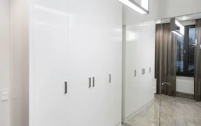 Garderoba w stylu eklektycznym z białymi szafami i lustrami, jasna podłoga.