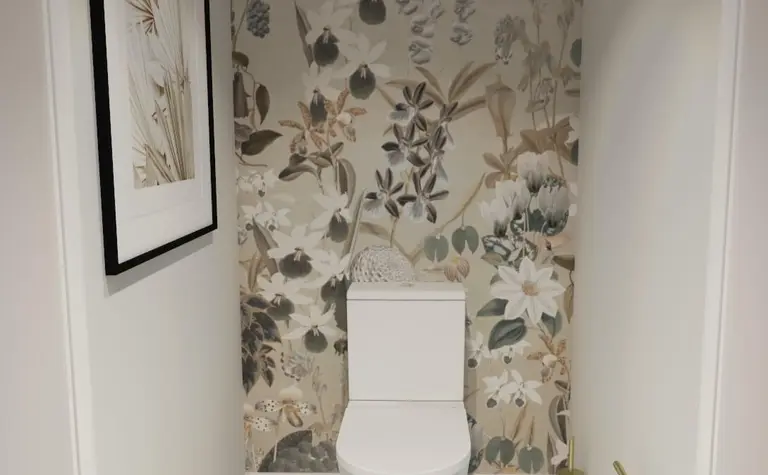 Toaleta z białą ceramiką, kwiecistą tapetą w stylu prowansalskim, czarno-biała podłoga.