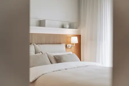 Sypialnia w stylu japandi z minimalistycznym wystrojem, białymi zasłonami i drewnianym łóżkiem.