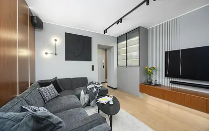Wnętrze salonu z szarym narożnikiem i drewnianymi detalami, styl industrialny i nowoczesny.