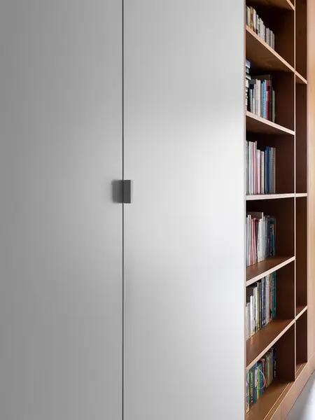 Nowoczesne wnętrze z minimalistyczną białą ścianą i drewnianą półką na książki.