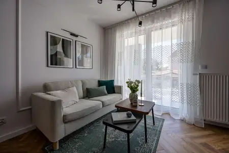 Współczesny salon z jasną sofą, zieloną wykładziną i drewnianymi akcentami.