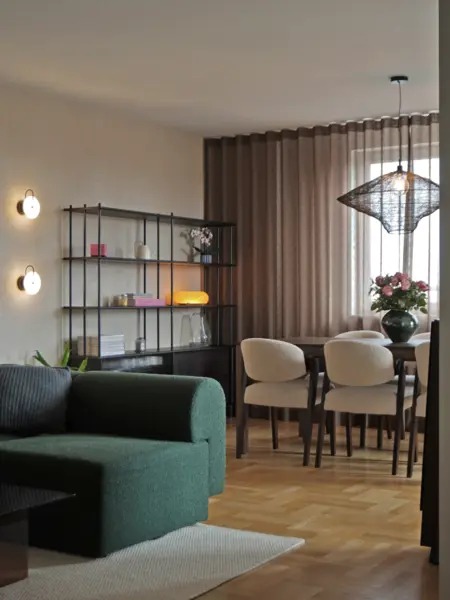Wnętrze jadalni z zieloną sofą, drewnianym stołem i nowoczesnymi lampami.