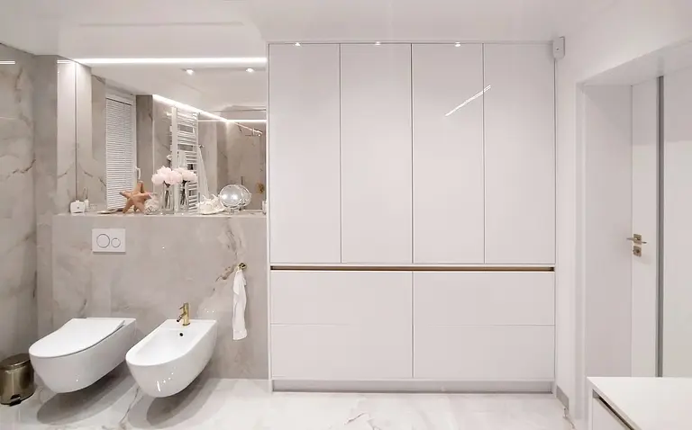 Nowoczesna łazienka glamour z białymi meblami i złotymi detalami.