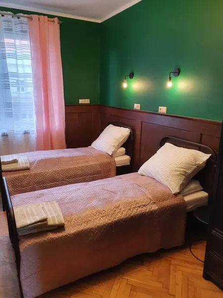 Pokój z dwoma łóżkami, zieloną ścianą i różowymi dodatkami w stylu tradycyjnym i vintage.