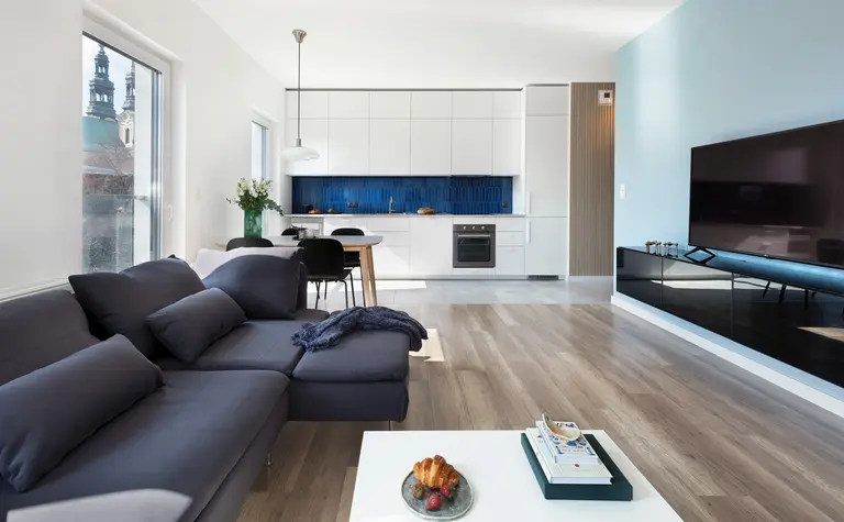 Wnętrze salonu z minimalistycznym designem, białą kuchnią i niebieskim tłem.