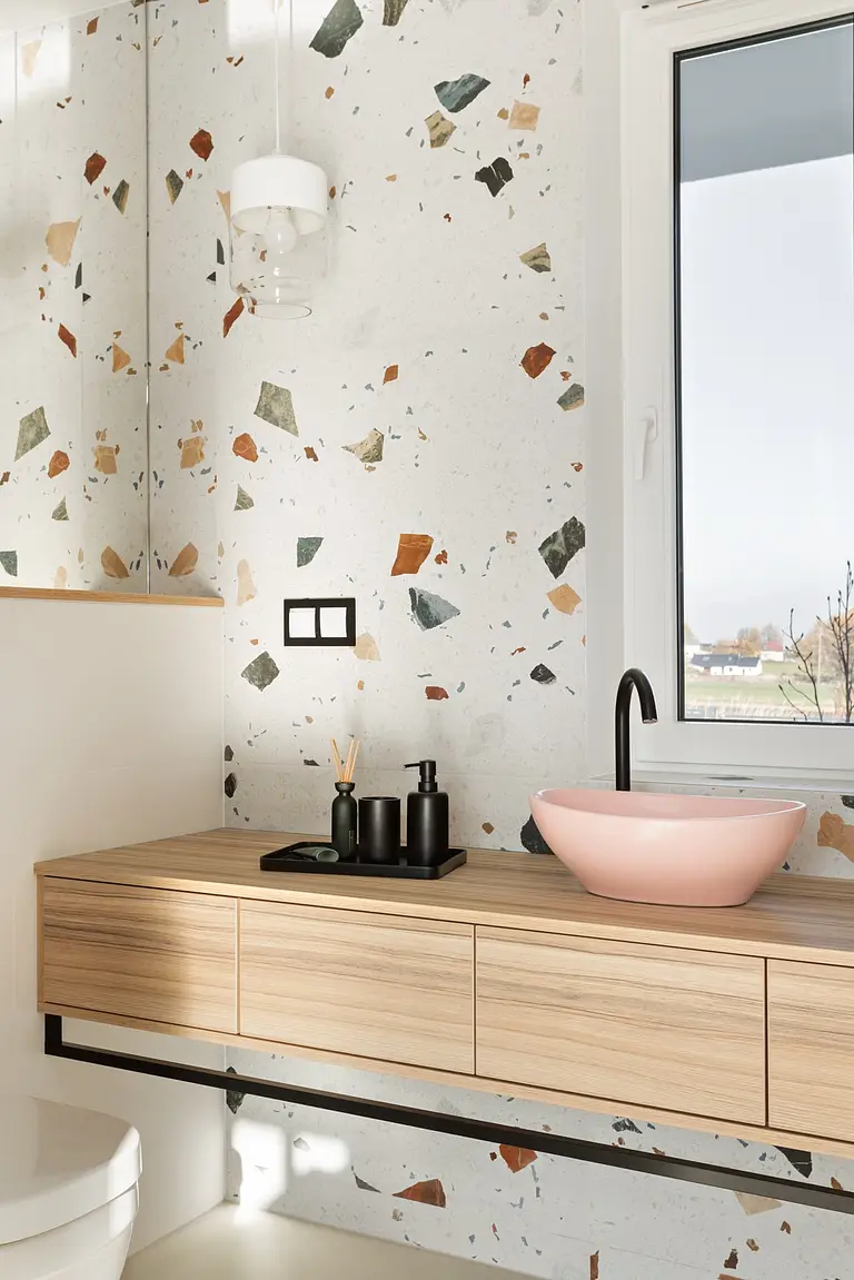Nowoczesna łazienka z elementami art deco, boho i glamour, z drewnianą szafką i różową umywalką.