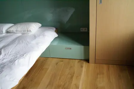 Sypialnia z eklektycznym i nowoczesnym designem, z drewnianą podłogą i jasnym łóżkiem.
