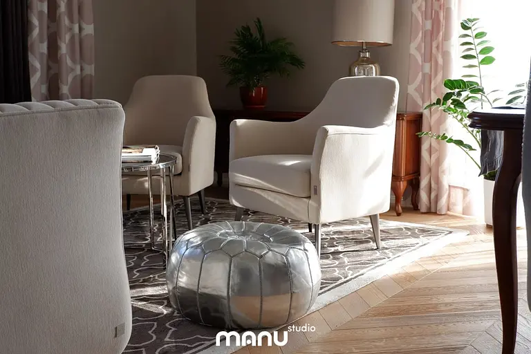 Eleganckie wnętrze salonu z jasnymi fotelami, metalowym pufem i rośliną. Styl tradycyjny.