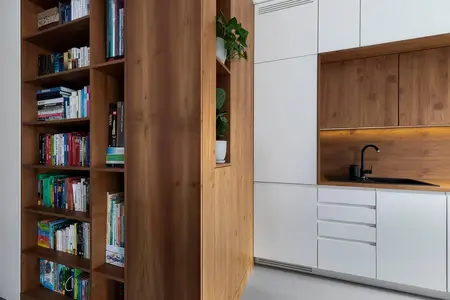 Minimalistyczne wnętrze kuchni z drewnianą półką i nowoczesnymi białymi meblami.