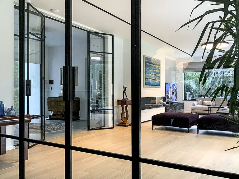 Wnętrze salonu minimalistycznego z dużymi oknami, drewnianą podłogą i roślinnością. Styl minimaluxe, quiet luxury.