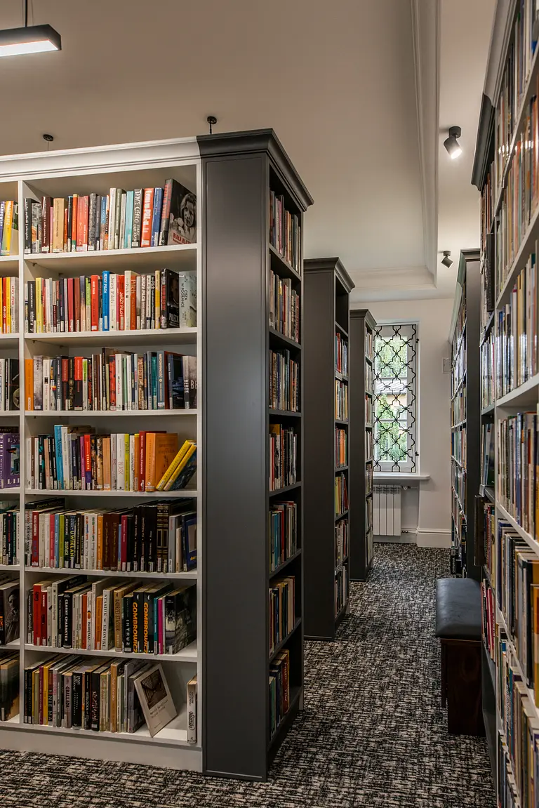 Wnętrze biblioteki z dużymi regałami, tradycyjny styl, książki na półkach, wygodne miejsce do czytania.