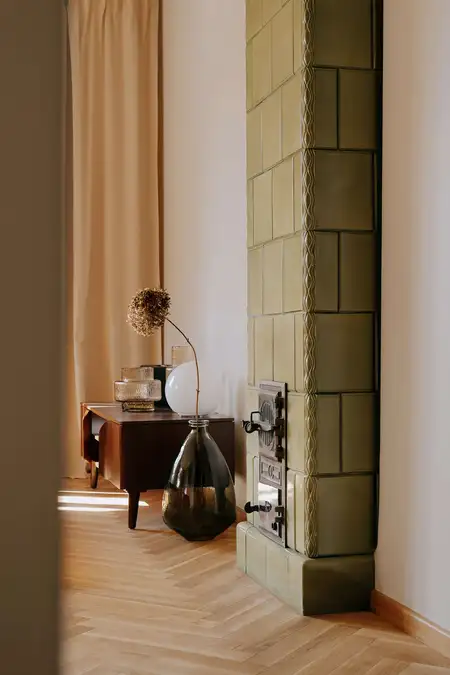 Wnętrze z zielonym piecem, drewnianą podłogą i minimalistycznymi dekoracjami.
