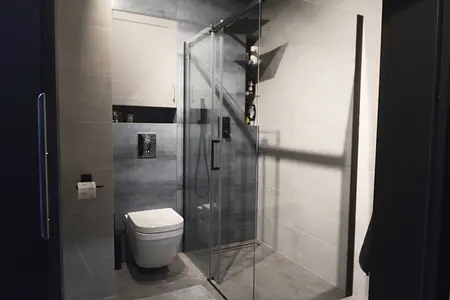 Wnętrze łazienki z minimalistycznym designem, szarymi płytkami i przezroczystą kabiną prysznicową.