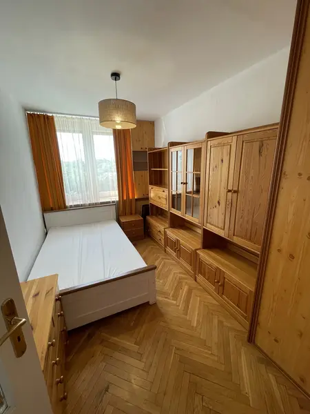 Sypialnia z drewnianymi meblami, białym łóżkiem i pomarańczowymi zasłonami.