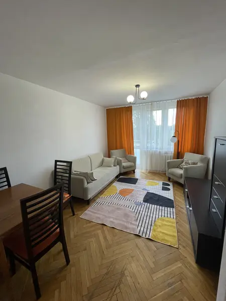 Wnętrze salonu z beżowymi meblami, pomarańczowymi zasłonami i kolorowym dywanem.
