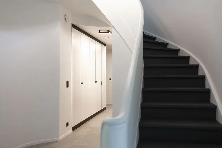 Przedpokój minimalistyczny z białymi szafkami i czarnymi schodami, styl minimaluxe, quiet luxury.