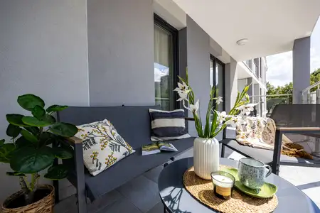 Współczesny balkon z szarym siedziskiem, zielonymi roślinami i dekoracyjnymi poduszkami.