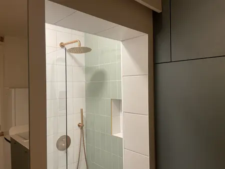 Nowoczesna łazienka z przeszkloną kabiną prysznicową, zielonymi płytkami i złotymi detalami w stylu skandynawskim.