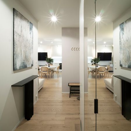Nowoczesny przedpokój z drewnianą podłogą, jasnymi ścianami i obrazami w stylu quiet luxury.