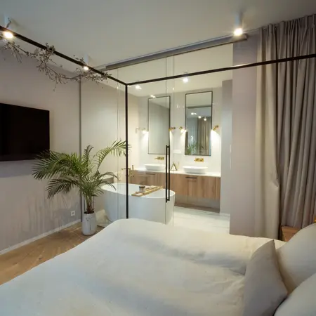 Sypialnia z łazienką, nowoczesne meble i rośliny w stylu quiet luxury.