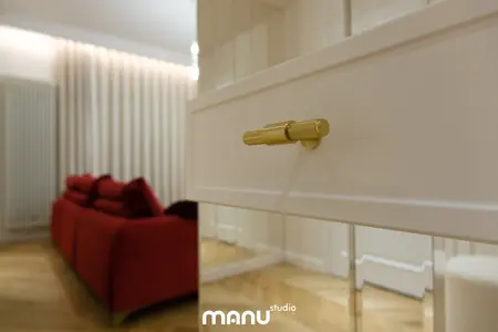Wnętrze salonu z białymi meblami, czerwonymi akcentami i drewnianą podłogą.