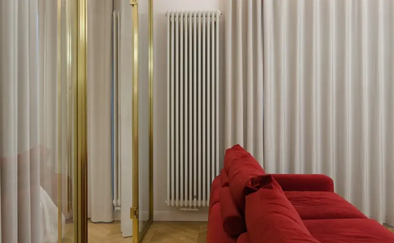 Wnętrze salonu z czerwoną kanapą, złotymi detalami i zasłonami.