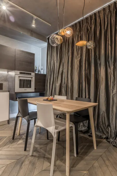 Nowoczesna kuchnia z drewnianym stołem i eleganckimi lampami wiszącymi, ciemnymi szafkami.