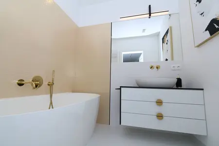 Wnętrze łazienki z białą wanną i złotymi detalami, styl minimaluxe i współczesny.