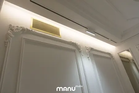 Stylowe wnętrze z białymi ścianami, złotymi akcentami i klasycznymi detalami.