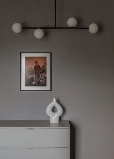 Minimalistyczne wnętrze z szaro-białą komodą, nowoczesnym oświetleniem i obrazem.