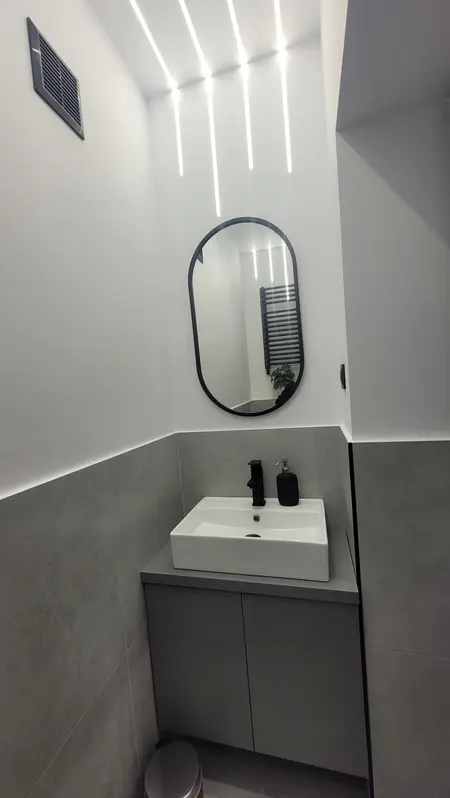 Nowoczesna łazienka z białą umywalką i szarymi płytkami w stylu minimalistycznym.