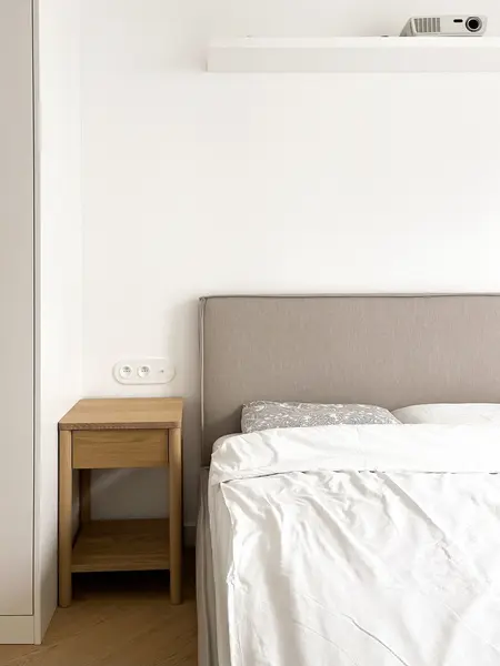 Minimalistyczna sypialnia z szarym wezgłowiem i drewnianą szafką, styl soft minimalizm