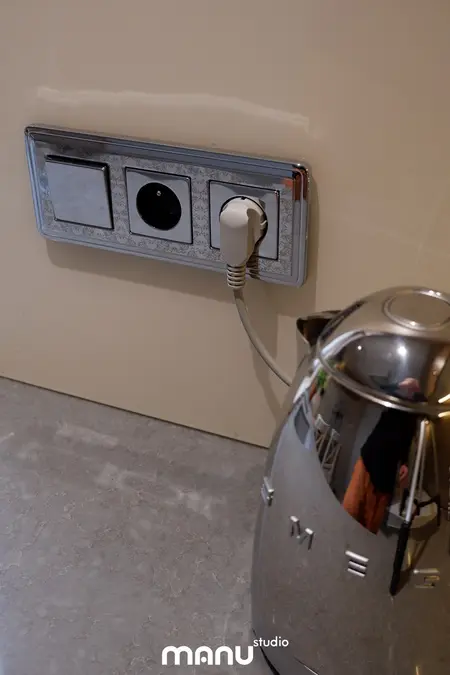 Gniazdko elektryczne na ścianie z metalowym czajnikiem w tradycyjnej kuchni.