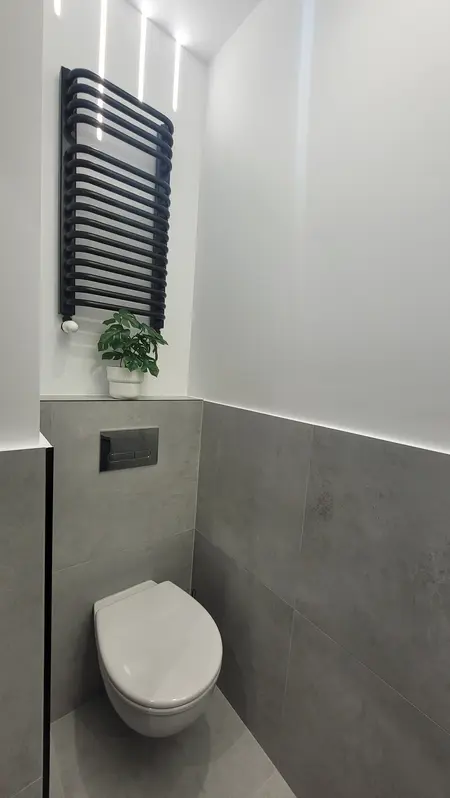 Minimalistyczna toaleta z szarymi płytkami i białą miską.